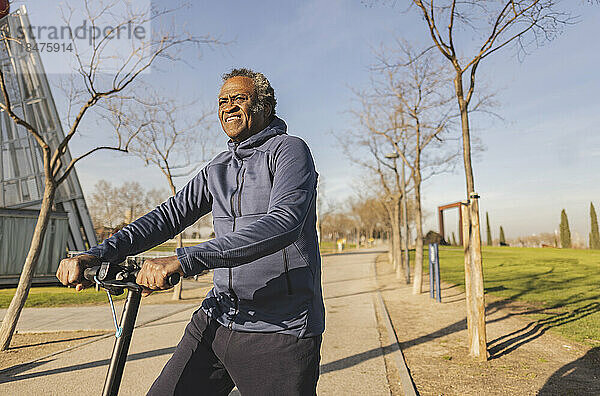 Nachdenklicher älterer Mann  der an einem sonnigen Tag einen Elektroroller fährt