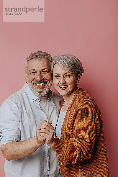 Glückliches reifes Paar  das vor rosa Hintergrund steht