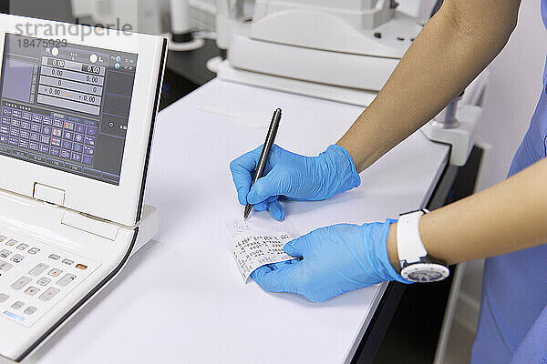 Augenarzt schreibt Testergebnisse am Schreibtisch in der Klinik auf Papier