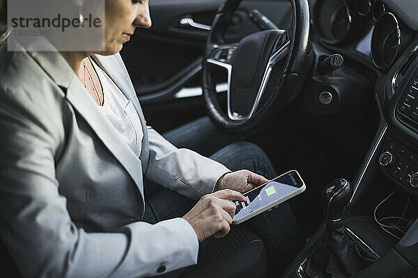 Reife Frau untersucht die Lade-App für Elektroautos auf ihrem Mobiltelefon