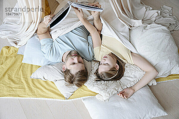 Vater und Tochter lesen zu Hause ein Buch auf einer Decke