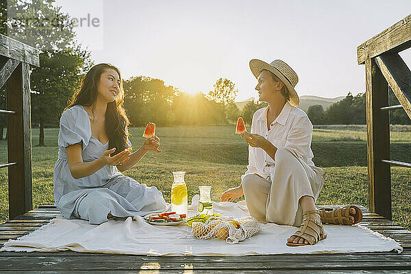 Glückliche Frauen halten Wassermelonenscheiben in der Hand und sitzen auf einer Picknickdecke