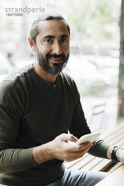 Lächelnder Mann benutzt Smartphone am Tisch im Café