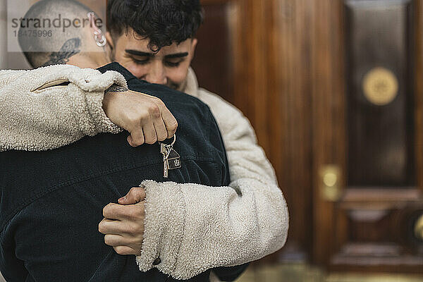 Gay couple with house key hugging each other in front of door