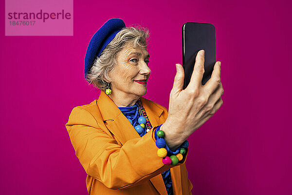Älterer Influencer macht Selfie mit Smartphone vor rosa Hintergrund