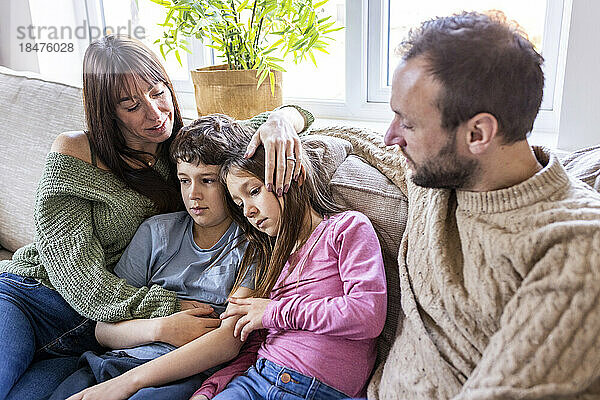 Glückliche Frau umarmt Kinder und Mann sitzt zu Hause auf dem Sofa