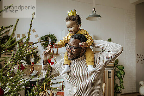 Glücklicher Mann mit Tochter  die zu Hause Weihnachtsschmuck berührt