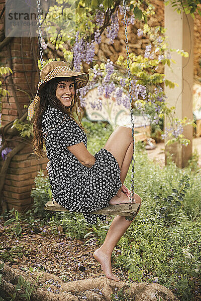 Lächelnde junge Frau sitzt auf einer Baumschaukel im Hinterhof