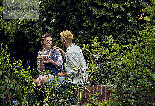 Junge Frau spricht mit ihrem Freund  der auf dem Zaun im Hinterhof sitzt