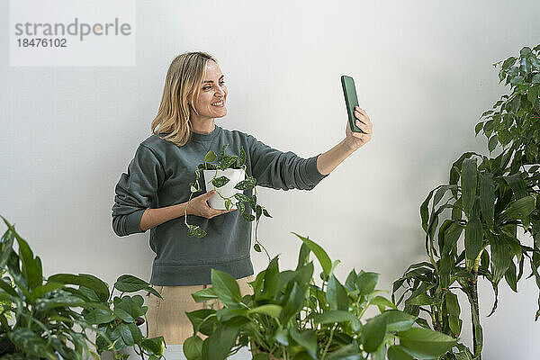 Glückliche Frau  die zu Hause ein Selfie mit einer Topfpflanze macht