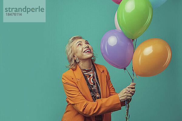 Glückliche ältere Frau hält bunte Luftballons vor türkisfarbenem Hintergrund