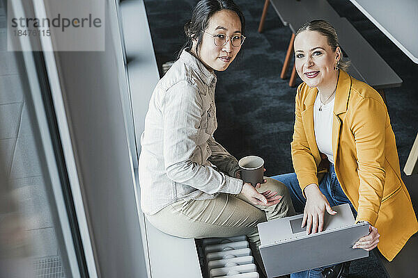 Lächelnde Geschäftsfrauen sitzen am Fenster im Büro