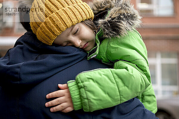 Tired boy wearing knit hat sleeping on father's shoulder