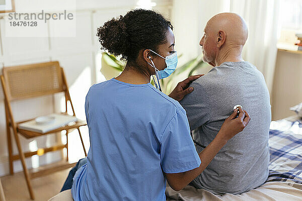 Krankenschwester hört zu Hause mit Stethoskop den Herzschlag eines älteren Patienten ab