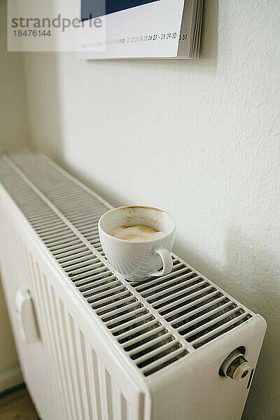 Eine Tasse Kaffee stand zu Hause auf dem Heizkörper in der Nähe der Wand