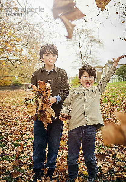 Fröhliche Jungen werfen Herbstblätter im Park weg