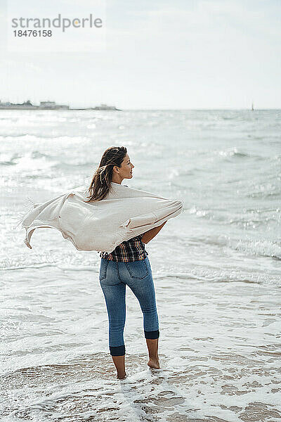 Frau mit Schal steht am Strand im Meer
