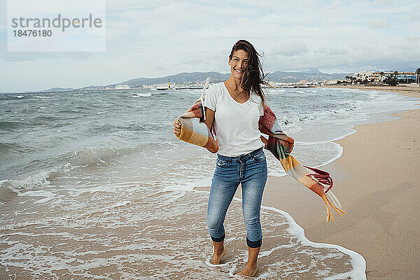 Lächelnde Frau  die in der Nähe der Küste am Strand steht