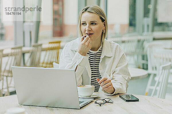 Geschäftsfrau mit Laptop am Tisch im Café  die Lippenstift aufträgt
