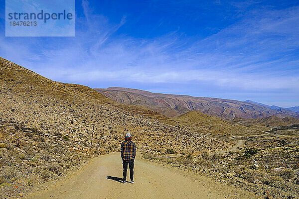 South Africa  Western Cape Province  Male hiker standing in middle of empty dirt road in Great Karoo