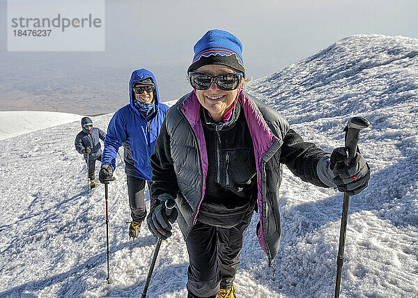 Lächelnde Wanderer wandern am Wochenende auf einem schneebedeckten Berg
