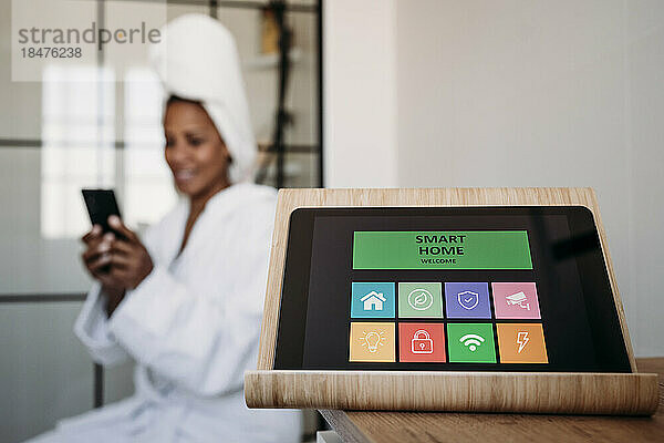 Hausautomations-App auf Tablet-PC mit Frau  die im Hintergrund ihr Smartphone nutzt