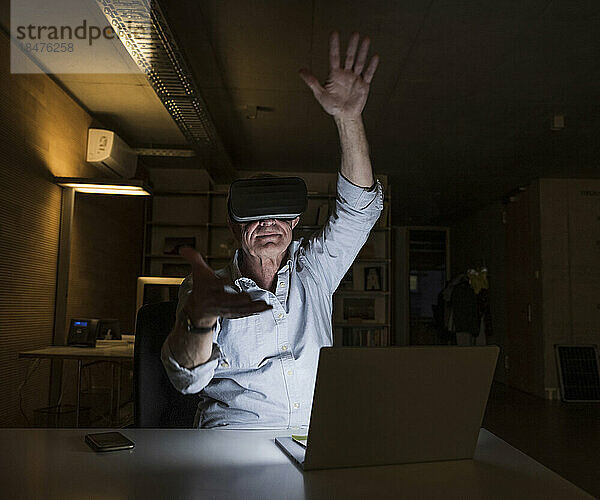 Geschäftsmann mit erhobener Hand und Virtual-Reality-Headset im Büro