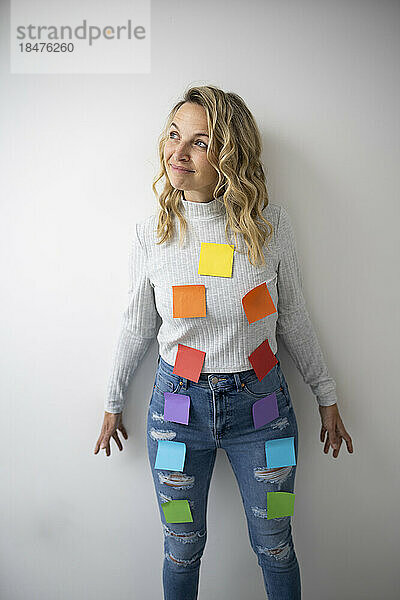 Thoughtful woman with colorful adhesive notes on body near wall