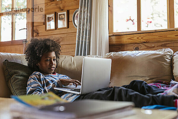 Junge benutzt Laptop und ruht zu Hause auf dem Sofa