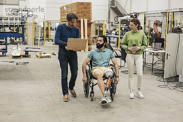 Ingenieur sitzt im Rollstuhl mit Kollegen in der Robotikfabrik