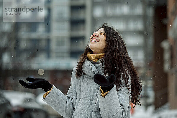 Glückliche Frau in warmer Kleidung genießt den Schneefall