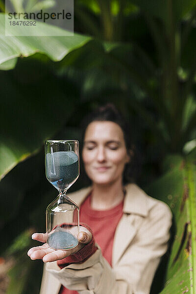 Frau mit Sanduhr steht vor einer Bananenstaude