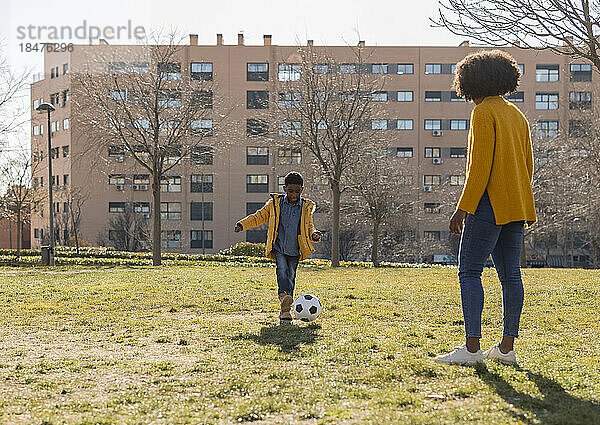 Boy playing soccer with mother in park on sunny day