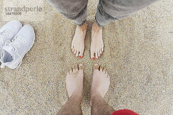 Man and woman standing barefeet on sand at beach