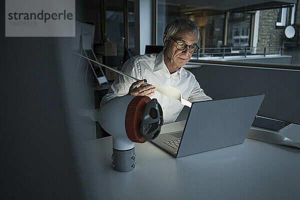 Ingenieur hält Rotorblatt in der Hand und benutzt Laptop im Büro