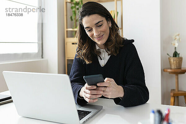 Lächelnde Geschäftsfrau benutzt Mobiltelefon am Schreibtisch