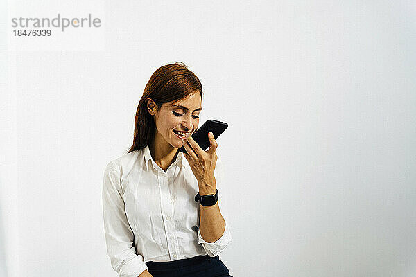 Glückliche Geschäftsfrau  die vor einer weißen Wand mit ihrem Smartphone spricht