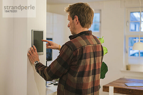 Mann benutzt Smart-Home-Gerät an der Wand zu Hause