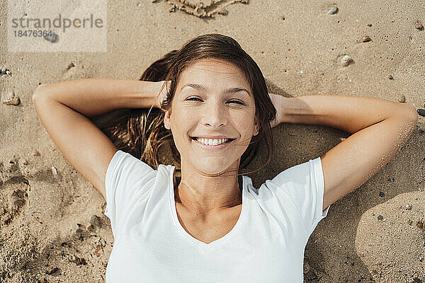Happy woman with hands behind head resting on sand