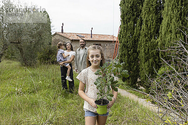 Mädchen hält Pflanze  Familie steht im Hintergrund
