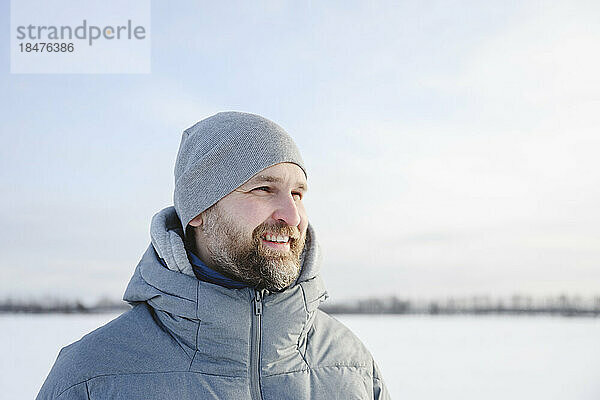 Glücklicher Mann mit Strickmütze im Winter unter dem Himmel
