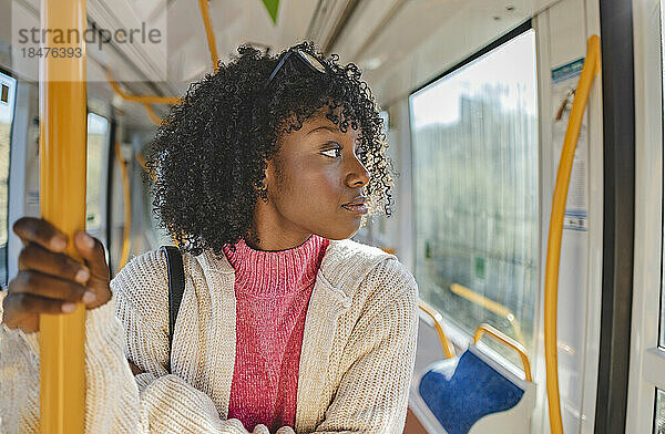 Junge Frau mit lockigem Haar steht in der Straßenbahn