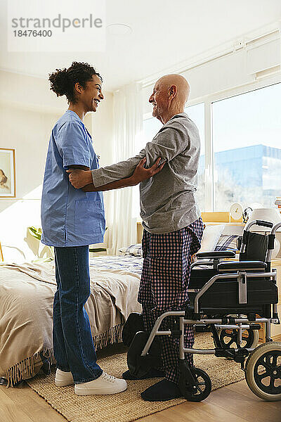Physiotherapeut unterstützt älteren Mann beim Stehen zu Hause