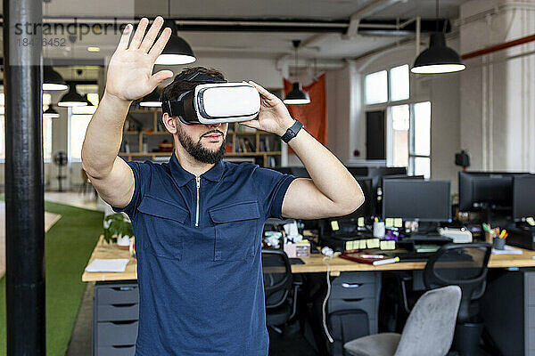 Junger Geschäftsmann mit VR-Brille gestikuliert im Büro