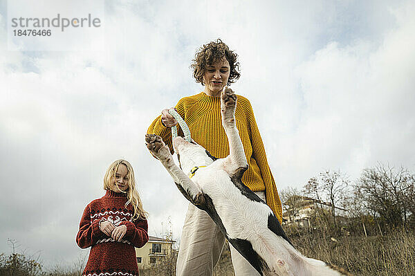 Mutter und Tochter spielen mit Bullterrier-Hund vor bewölktem Himmel