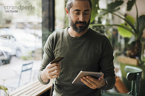 Bärtiger Mann mit Kreditkarte und Tablet-PC im Café