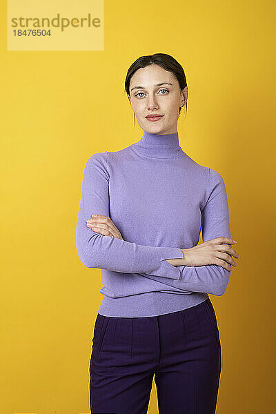 Confident young woman with arms crossed over yellow background