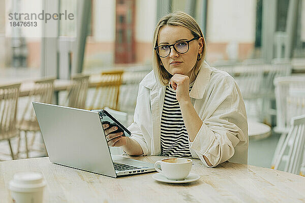 Geschäftsfrau mit Hand am Kinn und Smartphone im Café sitzend