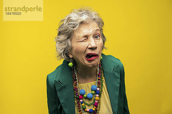 Ältere Frau macht lustige Gesichter vor gelbem Hintergrund