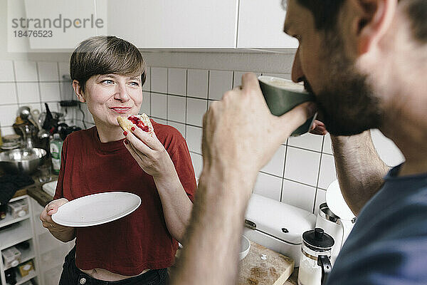 Lächelnde Frau schaut Mann an  der zu Hause in der Küche Kaffee trinkt